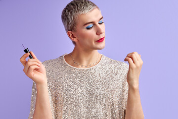 man blowing on his nails, drying fresh nail polish. Lgbt community. Transsexual gay isolated on purple background