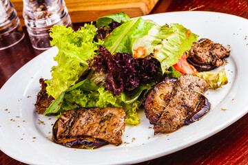Salad with eggplant, roast beef, lettuce and tomatoes on white plate