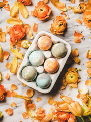 Obraz na płótnie Canvas Easter holiday background, texture and wallpaper. Flat-lay of colorful dyed Easter eggs in white ceramic egg holder over blooming orange flowers and white marble background, top view