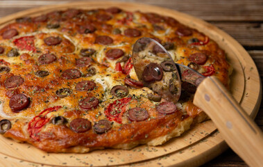 Delicious pizza being cut, reflected on the surface of the pizza cutter.