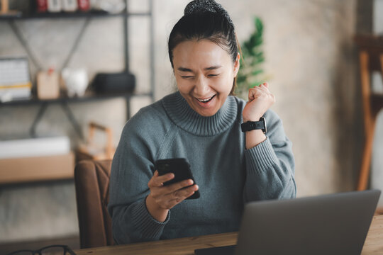 Excited Happy Asian Woman Looking At Phone Screen, Celebrating Online Win, Overjoyed Young Female Screaming With Joy, Holding Smartphone, Reading Good News In Unexpected Message Or Email