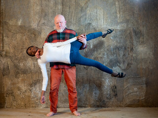 elderly man with gray beard in plaid shirt and red pants lifted beautiful African American girl in his arms and held her. Interracial marriage concept - Powered by Adobe
