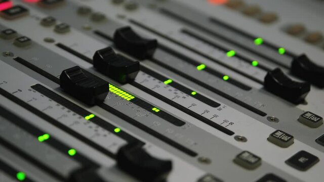 Sound engineer is moving levers of a multitrack mixing console in the control room during a recording session
