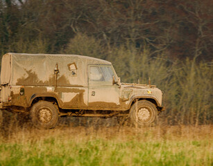 mud covered army land rover defender 4x4 driving along a track