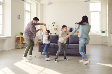 Happy young family with kids enjoying free time on weekend at home. Parents and children dancing and having fun in spacious living-room, celebrating moving into new house or rented apartment