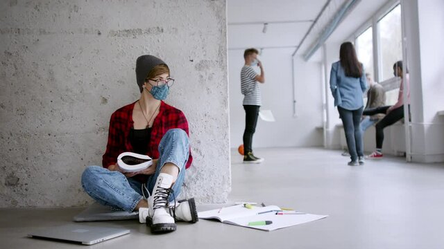 Young student with face mask sitting on floor back at college or university, coronavirus concept.