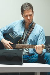 Obraz premium Man learns how to play the guitar. Remote online lesson.