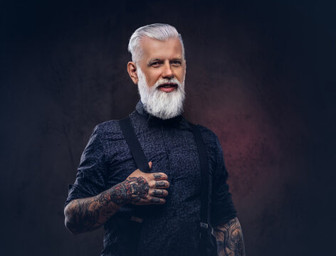 Dressed in modern and stylish clothing hipster grandfather looks at camera and smiles in dark background.