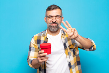 adult man smiling and looking friendly, showing number three or third with hand forward, counting...