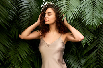 woman in beige elegant silk dress posing in tropical garden. natural beauty, perfect face, bronze skin