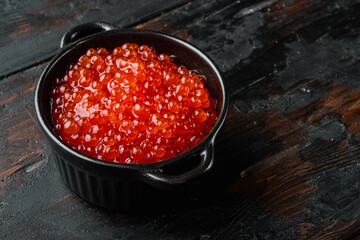 Black bowl with delicious red caviar, on old dark  wooden table background  with copy space for text