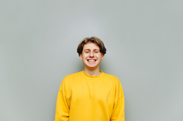 Portrait of a guy in a yellow sweatshirt on a gray background looks at the camera with a smile on...