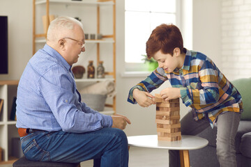 Grandfather and grandson play a game of jenga and take turns pulling bricks out of a wooden tower. Mature man with a small child have fun playing a fun board game at home.