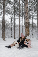 mother and daughter playing with snow in forest and drinking tea 