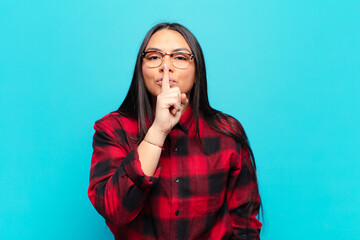 latin woman looking serious and cross with finger pressed to lips demanding silence or quiet,...