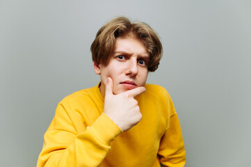 Close-up portrait of a funny guy in a yellow sweatshirt looks intently at the camera with a pensive...