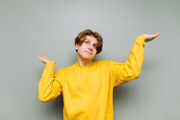 Portrait of puzzled guy in casual clothes on a gray wall background, spreads his arms away from confusion. Isolated.