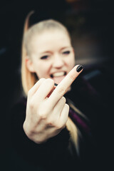Pretty blond girl on dark background, flipping the bird at the camera