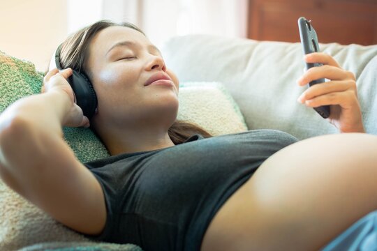 A relaxed pregnant woman listening to music with headphones and a phone. Happy people enjoying audio apps.