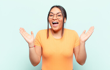 latin woman feeling happy, excited, surprised or shocked, smiling and astonished at something...