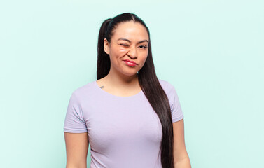 latin woman looking happy and friendly, smiling and winking an eye at you with a positive attitude