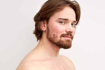 smiling shirtless man having bristle looking at camera, young caucasian male model isolated over white background. side view portrait