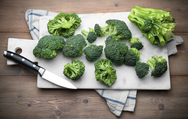 Sicilian broccoli cut into pieces with white marble cutting board and knife on wooden background,...