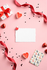 Valentines Day creative layout with blank paper card, gift box, red ribbon, confetti on pink background. Love, romance concept.