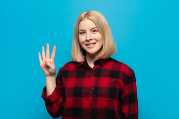 blonde woman smiling and looking friendly, showing number four or fourth with hand forward,...