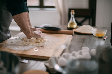 Fototapeta na wymiar A male chef prepares noodle dough at home in the kitchen. Close up of hands with flour and dough