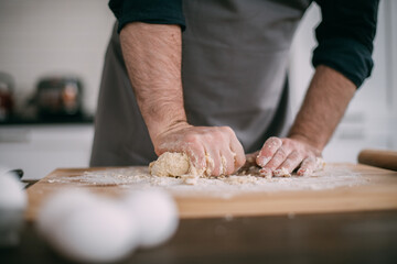 A male chef prepares noodle dough at home in the kitchen. Close up of hands with flour and dough