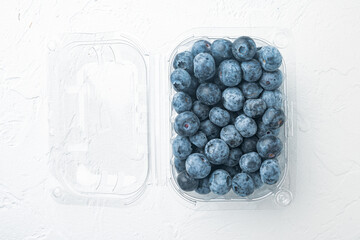 Blueberries in clear plastic tray, on white background, top view flat lay