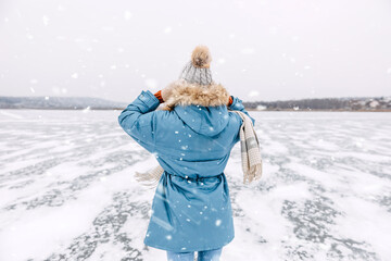 Back view of a woman standing on a frozen lake on a cold winter day in snow fall.