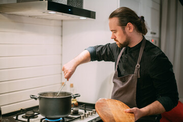 A male cook is cooking at the stove at home in the kitchen
