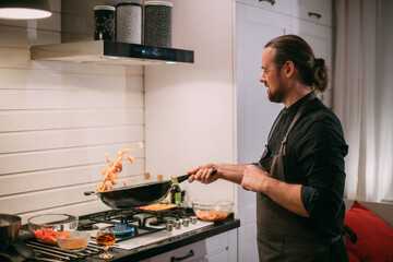A male cook is cooking at the stove at home in the kitchen
