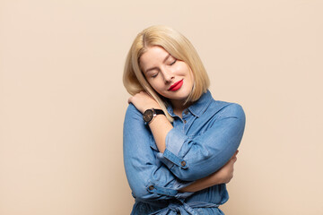 blonde woman feeling in love, smiling, cuddling and hugging self, staying single, being selfish and...