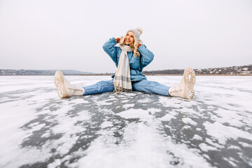 Cheerful young blonde woman sitting on frozen lake in winter.