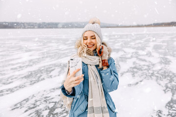 Fototapeta na wymiar Cheerful young blonde woman taking a self portrait standing on frozen lake in winter.