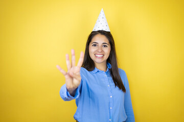 Young caucasian woman wearing a birthday hat over isolated yellow background showing and pointing...