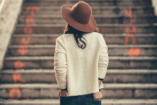 mujer de espaldas con sombrero frente a una escalera de ciudad y texto te quiero. 