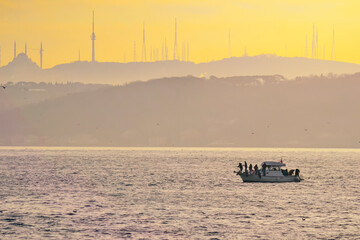 Bosphorus with small boat floats with people fishing in a beautiful sunset view of Istanbul city in the evening.