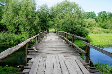 Fototapeta na wymiar old wooden bridge across the river on a beautiful summer day and the clear water of the river and green trees