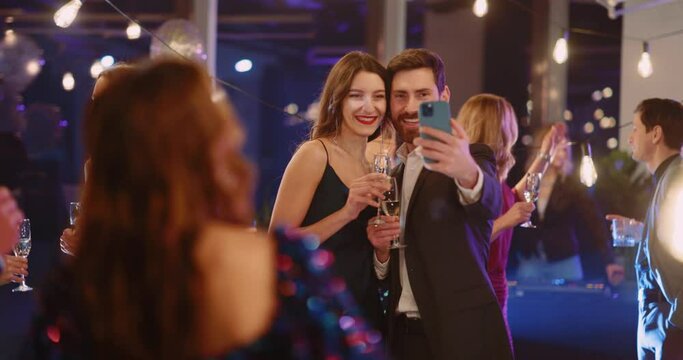 Handsome caucasian couple of married woman man taking family photo picture in smartphone while hanging out on public social corporate party indoors.
