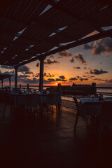 Sunset over water from the dining area of a sea front restaurant in southern Italy.Tables ready for service, silhouettes, amazing colored sky and sea.
