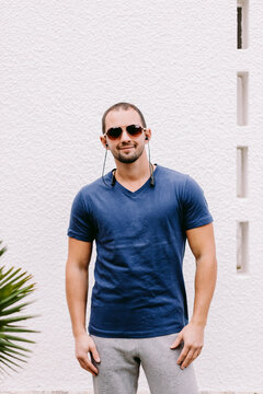 Man In Blue T-shirt Mockup Wearing Sunglasses And Listen Music. Man In Blank Blue T-shirt V Collar And Shirt And Headphones, Front View Outdoors. Design Men T Shirt Template And Mock-up For Print 