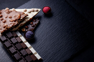 Three types of chocolate - black, milk and white with luxury handmade chocolates on a black background with copy space