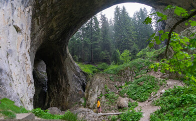 Fototapeta na wymiar Lonely woman standing on wonderful bridge in Bulgaria. Famous and mysterious open wide cave. Magnificent rock formation and girl walking on a tour alone in vacation. stone arch with ecosystem