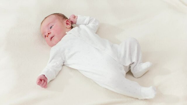 View from abov eon adorable 1 months old baby boy lying on white blanket on bright sunny day.