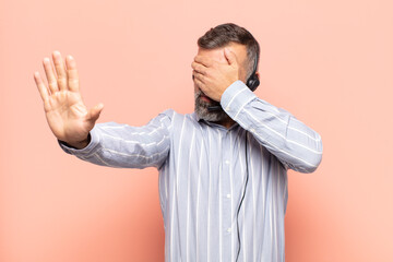 adult handsome man covering face with hand and putting other hand up front to stop camera, refusing...