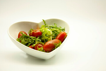 Mix of lettuce, carrots and red cherry tomatoes served in a ceramic heart shaped bowl